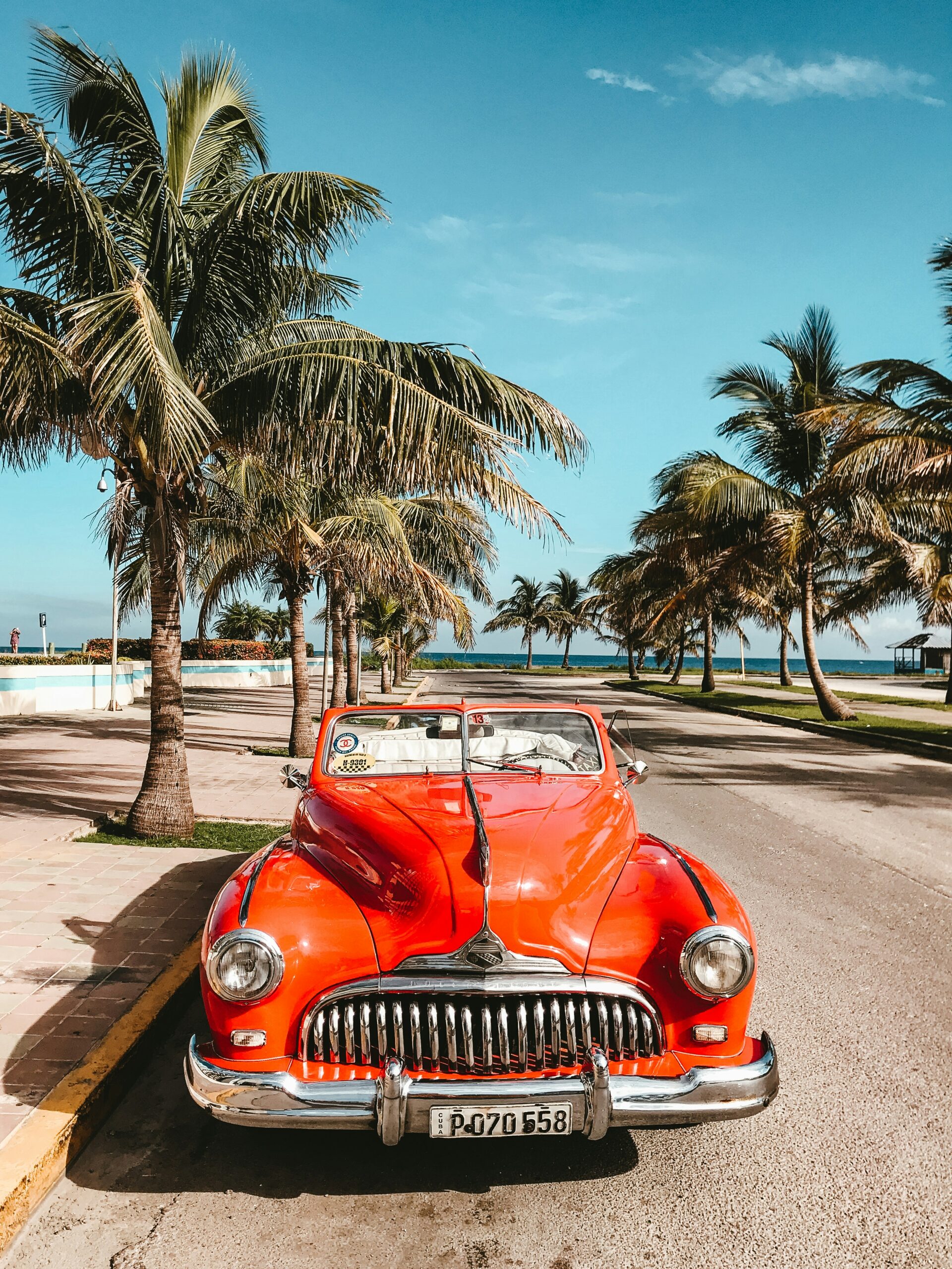 stephan-valentin-6NT7jy6OU9I-unsplash Red convertible parked on a palm lined street
